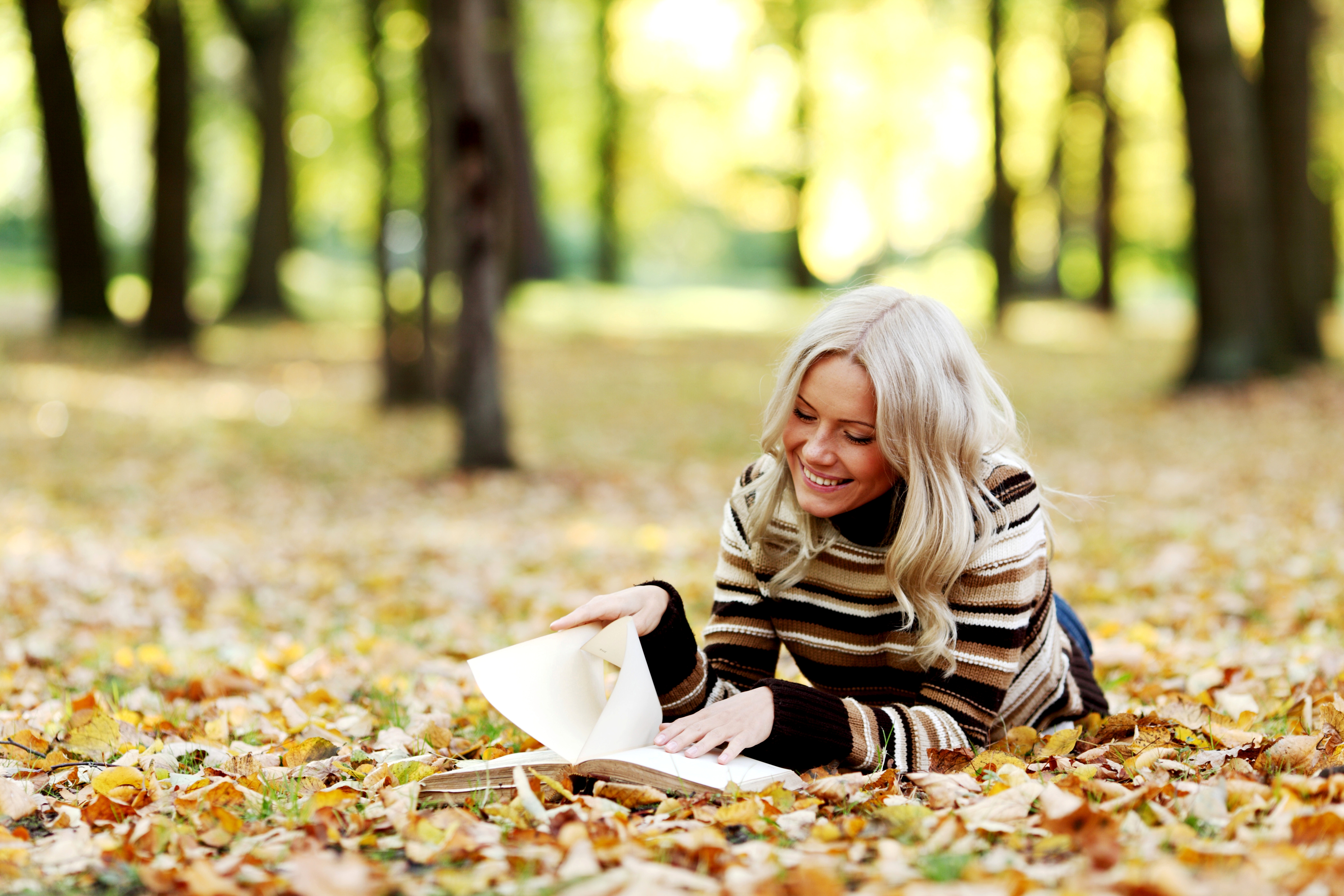 Голая блондинка в парке сидит на желтых листьях